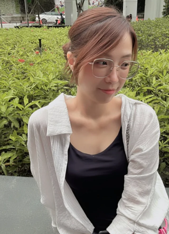 戴著眼鏡的 Grace，坐在綠色植物前